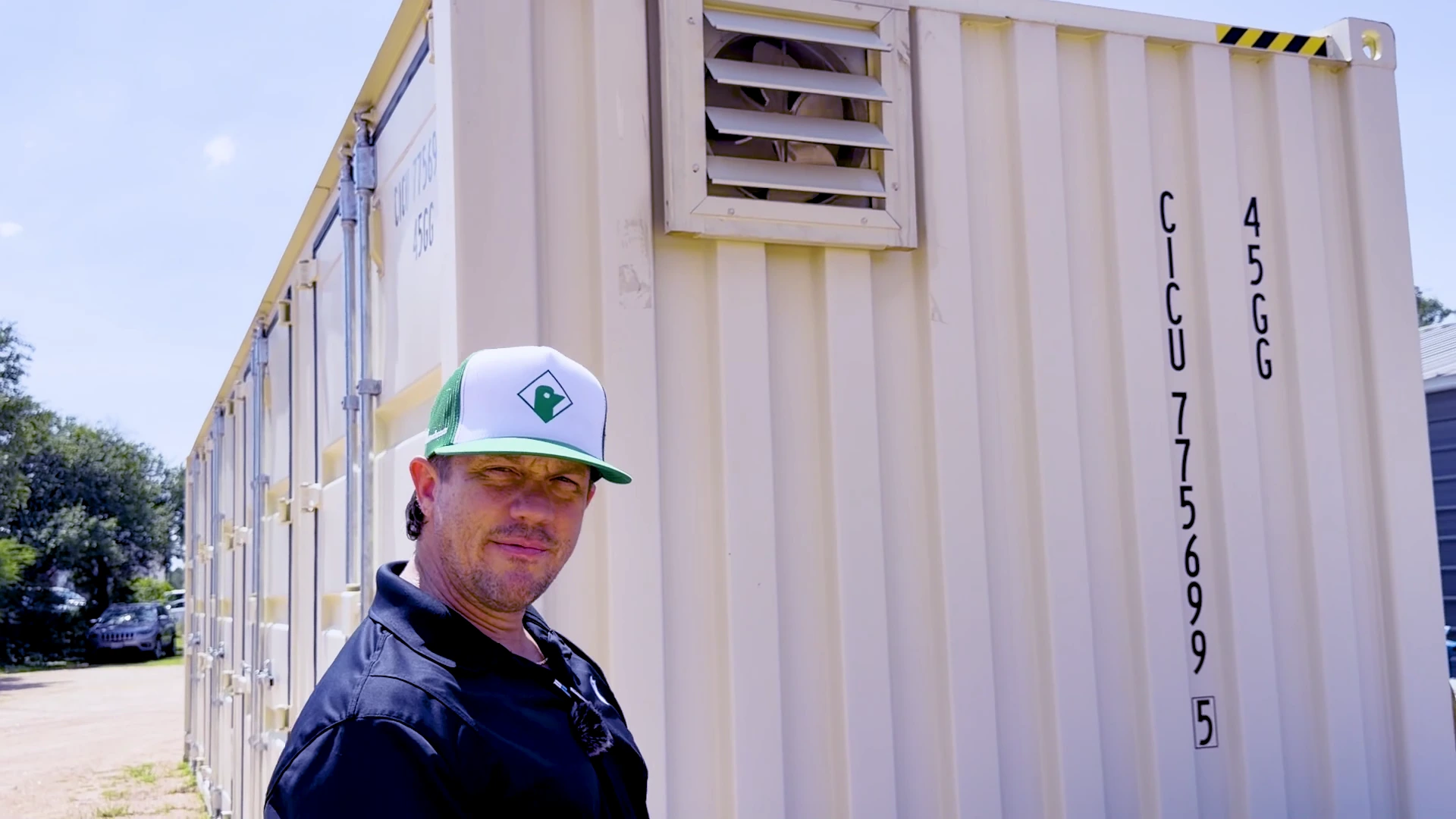Luke Secora pointing to an Attic Breeze powered fan behind a wall louver