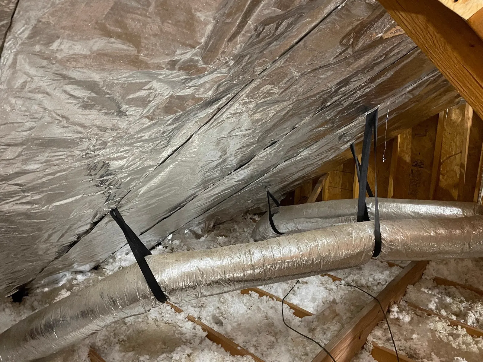 Reflective radiant barrier installed under a roof deck in a Central Texas attic, with ductwork and cellulose insulation visible below